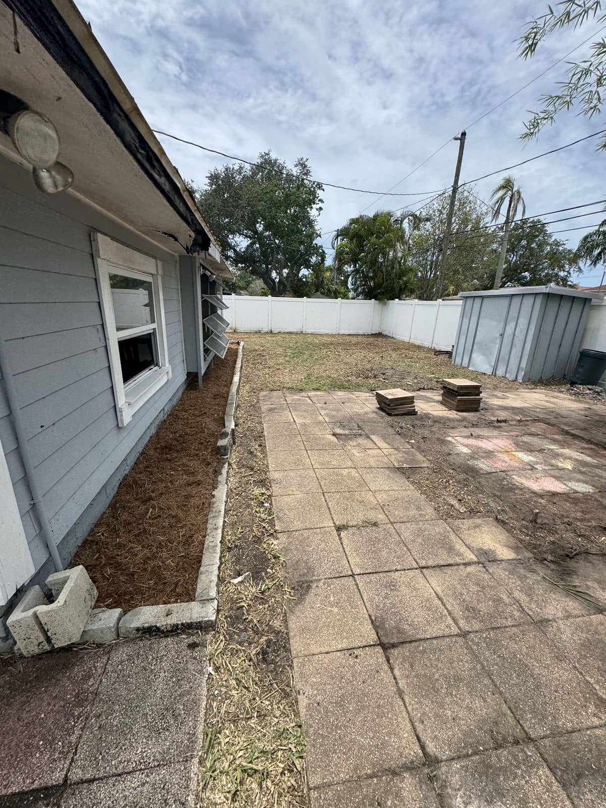 After photo of the same backyard cleared up with a clean paver patio and a fresh bordered planting bed.